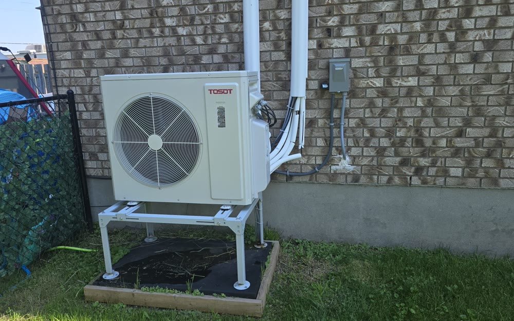 Outdoor heat pump condenser installed on a levelled stand beside an Ottawa home
